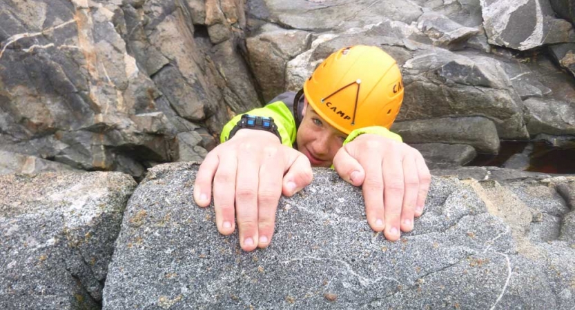 A person wearing a helmet grips a rock with both their hands. 